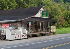 an old ice cream shop sitting on the side of a road next to a forest