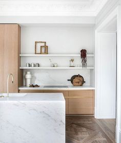 a kitchen with white marble counter tops and wooden cabinetry, along with open shelving