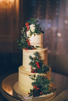 a three tiered wedding cake decorated with greenery and berries