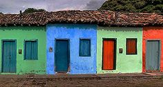 colorfully painted houses line the street in front of a hill side house with a thatched roof