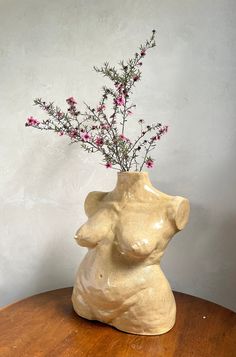 a vase with pink flowers in it sitting on a wooden table next to a white wall