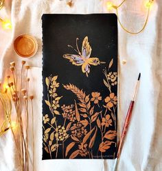 an image of a book with flowers and butterflies on it next to some paintbrushes