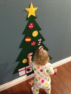 a toddler standing in front of a christmas tree made out of paper and buttons