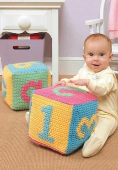 a baby sitting on the floor next to two crocheted blocks