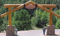 two people walking under a wooden structure in the middle of a road with trees behind them