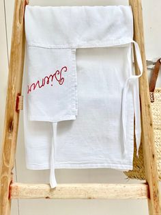 two white towels with red writing on them sitting on top of a wooden step ladder