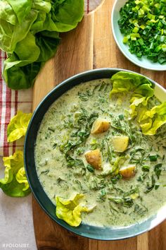 a bowl of soup with lettuce and other vegetables on the table next to it