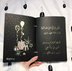 a hand holding an open book with writing on the cover and balloons in the background