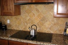 a kitchen counter with a tea kettle on it next to some brown cabinets and granite counter tops