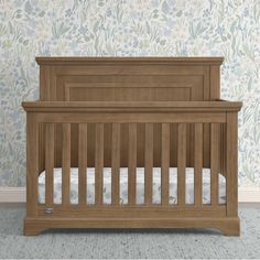 a wooden crib in front of a floral wallpaper