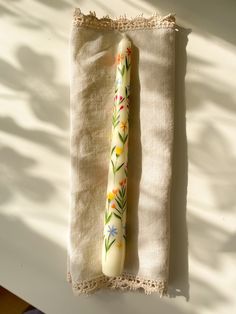 a white candle sitting on top of a table next to a piece of cloth with flowers painted on it