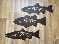 three metal fish cutouts sitting on top of a wooden floor