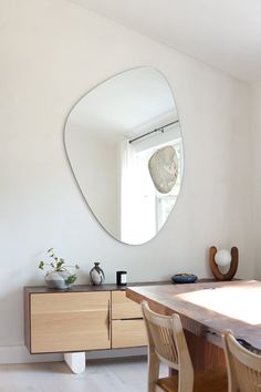 a table with chairs and a round mirror on the wall in a white walled room