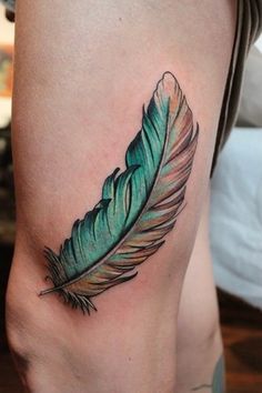 a woman's leg with a green and brown feather tattoo on the side of her thigh