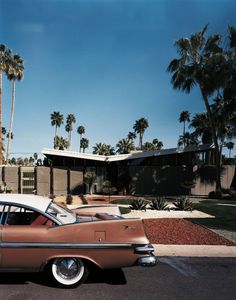 an old car is parked in front of a house with palm trees on the side