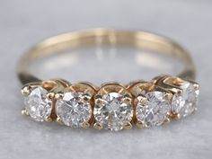 This wedding band features a row of bright and sparkling diamonds, each set into protective four-prong settings. Crafted of 14 karat yellow gold, this ring is a classic design that will be timeless for years to come. Metal: 14K Yellow Gold Gem: 5 Diamonds totaling 1.00 Carat, H in Color, SI2 in ClarityGem Measurements: 4.0 mm, Round Ring Size: 8 Marks: “14K” Stamped on the inside band Wedding Ring Sets Round, Wedding Band Yellow Gold, Yellow Gold Diamond Wedding Band, Jewels Diy, Jewelry Stacking, Australian Sapphire, Gold Diamond Band, Unusual Rings, Diamond Anniversary Rings