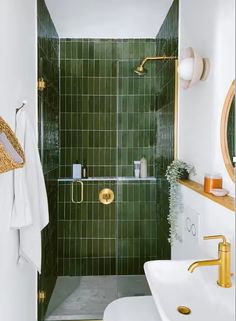 a green tiled bathroom with gold fixtures and white sink, mirror, and shower stall