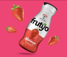 a bottle of fruity yogurt with strawberries flying around it on a pink background