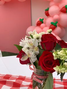 a vase filled with red roses and white flowers on top of a checkered table cloth