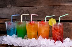 five different types of drinks lined up on ice with straws and lemon wedges