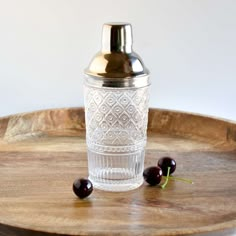 an old fashioned cocktail shaker and two cherries on a wooden tray