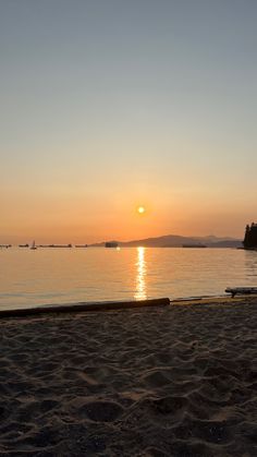 the sun is setting over the water and sand on the beach with boats in the distance