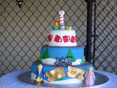 a three tiered cake decorated with fondant and paper decorations on a table in front of a chain link fence