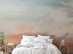 a bed with white sheets and pillows in front of a wall mural that has clouds painted on it