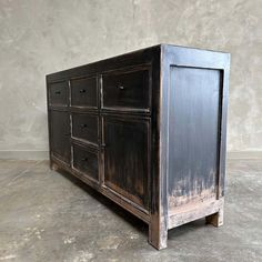 an old black dresser is sitting on the floor in front of a gray wall and concrete floor