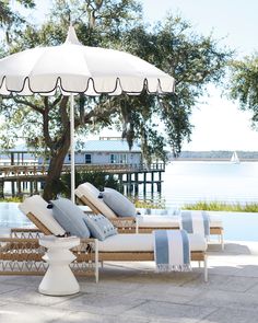 two chaise lounges under an umbrella near the water