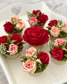 cupcakes decorated with red and pink flowers on a white tray in the shape of roses