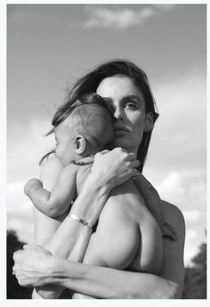 a woman holding a baby in her arms with the sky behind her and clouds overhead