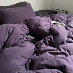 an unmade bed with purple sheets and pillows