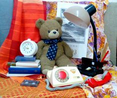 a brown teddy bear sitting on top of a bed next to a lamp and books