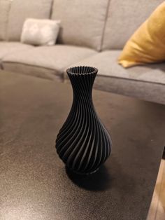 a black vase sitting on top of a table next to a gray couch and pillows