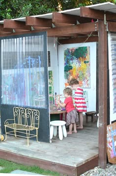 two children are playing outside on the deck in front of an art studio with their artwork