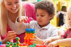 a woman and two children playing with colorful beads on a table in a playroom