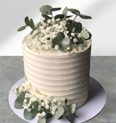 a cake with white flowers and greenery on top is sitting on a platter