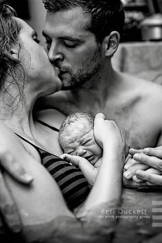 a man and woman are kissing while holding a baby in their arms, black and white photograph