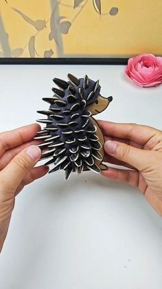 a person holding a fake hedgehog toy next to a pink flower on a table