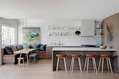 an open kitchen and living room with wood flooring, white counter tops and wooden bar stools