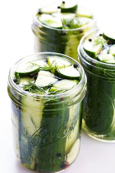 three jars filled with pickles and cucumbers on top of a white table