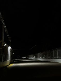 an empty parking lot at night with lights on the fence and stairs leading up to it