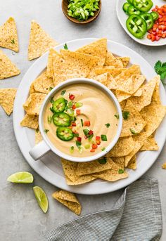 a white plate topped with guacamole surrounded by tortilla chips and sliced jalapenos