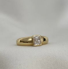 a yellow gold ring with a princess cut diamond in the center, sitting on a white cloth