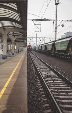 two trains are parked on the tracks at an empty train station, one is green and the other is yellow