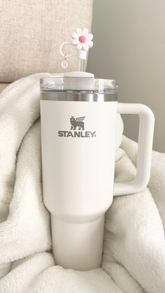 a white travel mug sitting on top of a blanket next to a flower in a vase