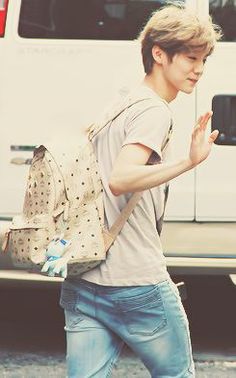 a young man walking across a parking lot with a backpack on his back and one hand in the air