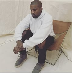 a man sitting on top of a chair with his hands in his pockets and wearing boots