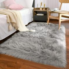 a white bed sitting next to a gray rug on top of a hard wood floor